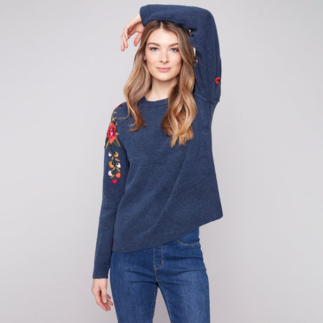 Woman wearing a blue sweater with floral embroidery on a gray background