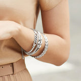 Silver bracelets on a person's wrist with a neutral background