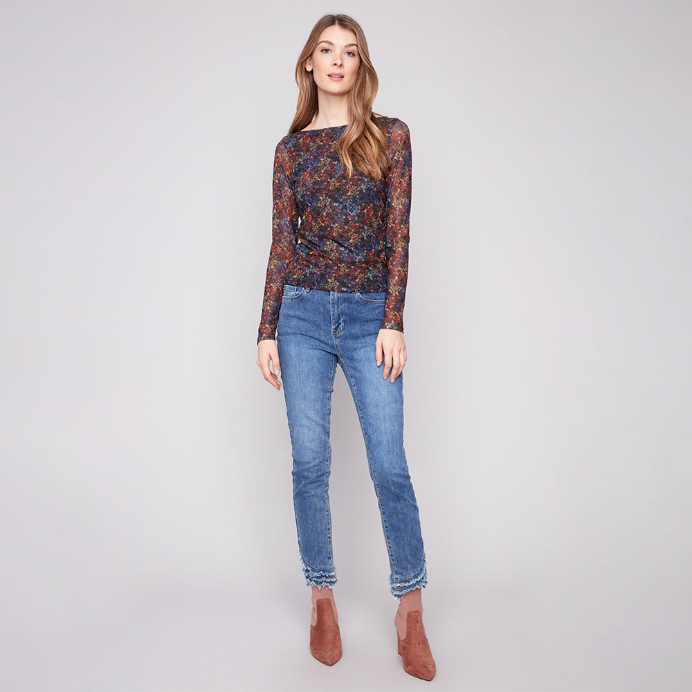 Woman wearing a patterned long-sleeve top and blue jeans on a plain background