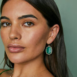 Close-up of a woman wearing green earrings against a green background