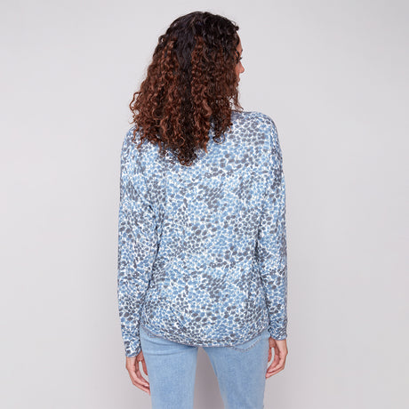 Person wearing a blue patterned shirt and light blue jeans on a plain background
