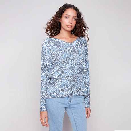 Woman wearing a blue floral long-sleeve top and light blue jeans on a gray background