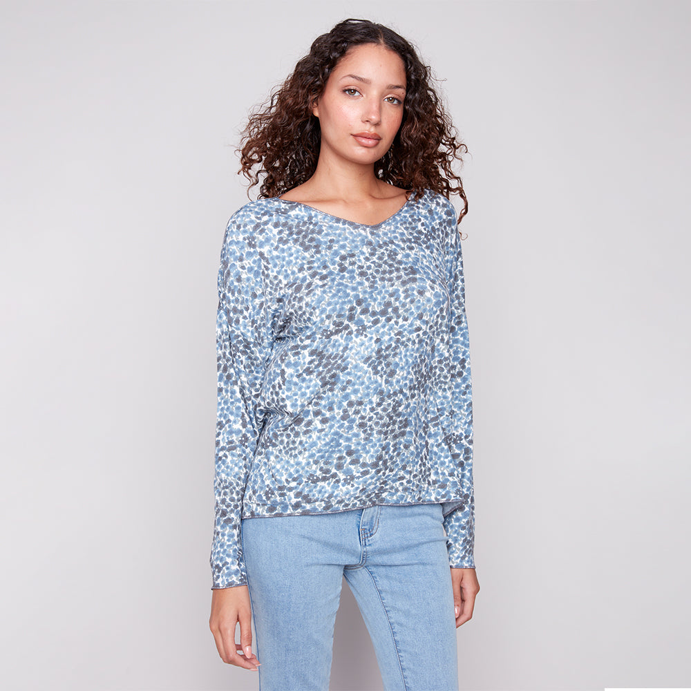 Woman wearing a blue floral long-sleeve top and light blue jeans on a gray background