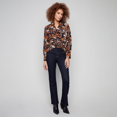 Woman wearing a patterned blouse and dark jeans on a gray background