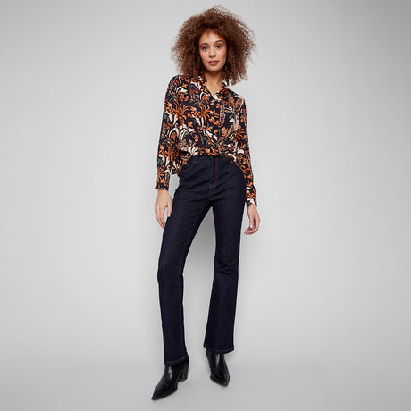 Woman wearing a patterned blouse and black pants on a gray background