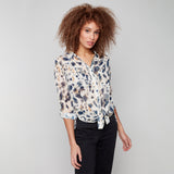 Woman wearing a patterned blouse and black pants against a gray background