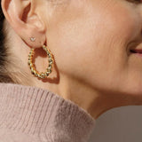 Close-up of a person wearing gold hoop earrings with a neutral background