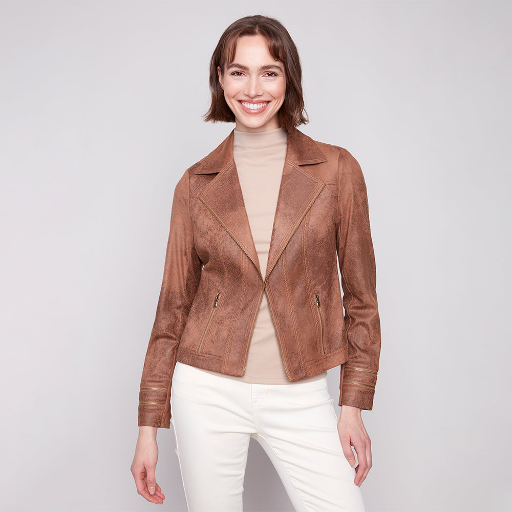 Woman wearing a brown leather jacket over a beige top and white pants on a light gray background