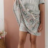 Person wearing a floral skirt and light gray t-shirt against a pink background