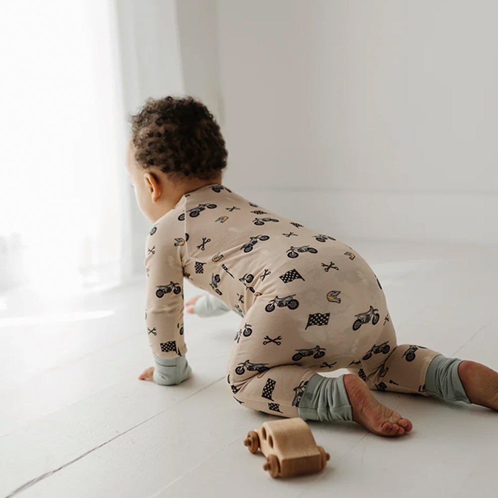 Child in patterned pajamas playing with a toy car on a light floor.