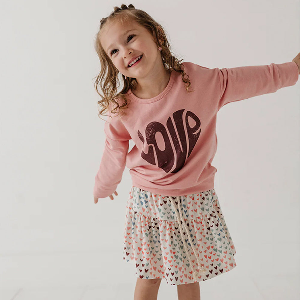 Child wearing a pink sweatshirt with 'LOVE' and a patterned skirt on a plain background