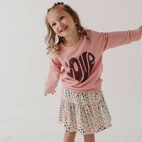 Child wearing a pink sweatshirt with 'LOVE' and a patterned skirt on a plain background