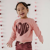 Child wearing a pink sweatshirt with a heart design in a heart-patterned room
