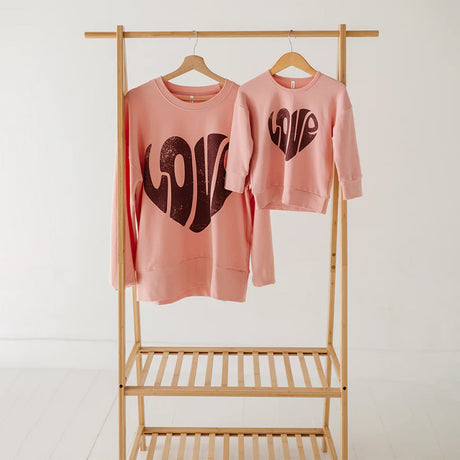 Two pink sweatshirts with 'LOVE' text on a wooden rack against a white background