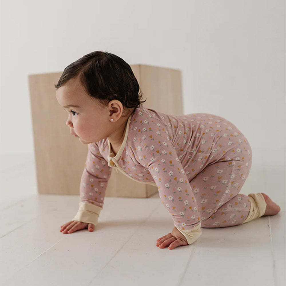 Baby in pink floral pajamas crawling on a white floor.