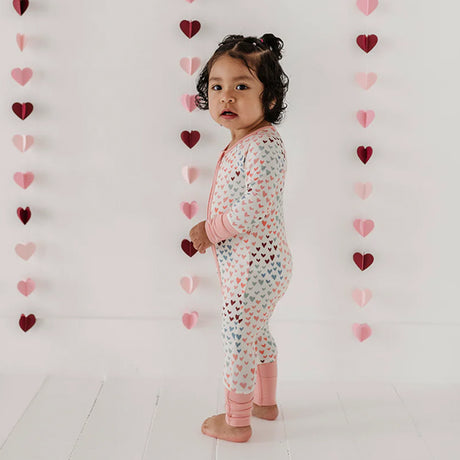 Child wearing a heart-patterned onesie in front of a heart-themed wall.