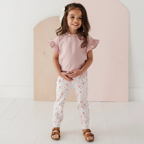 Young girl wearing a pink top and floral pants standing against a light background