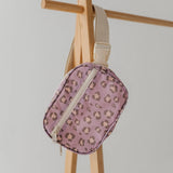 A small zippered pouch with a pink leopard print pattern and a beige adjustable strap, hanging from a wooden display stand against a light gray background.