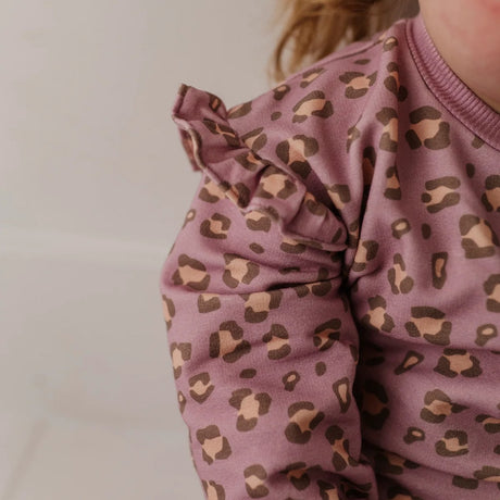 Close-up of a child wearing a dusty mauve long-sleeve top with a brown and beige leopard print, featuring ruffled detailing on the shoulder.