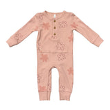 A baby's long-sleeve ribbed jumpsuit in a dusty pink color, decorated with a pattern of simple pink and brown flower outlines. It features a button-up front with three wooden buttons.