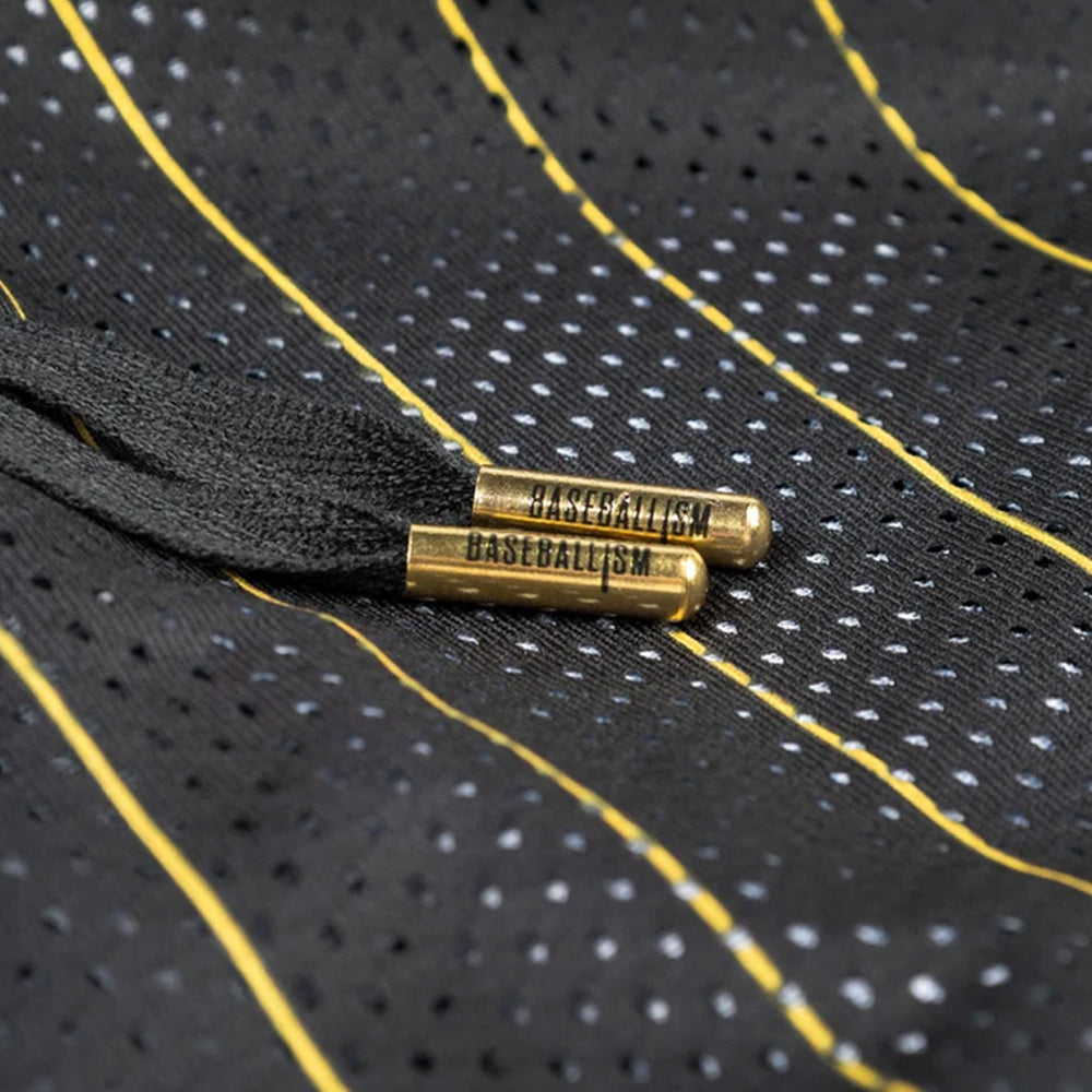 Close-up of a black mesh drawstring bag with yellow and white dotted stripes, featuring brass grommets engraved with the word 'GASTBULLISM'.