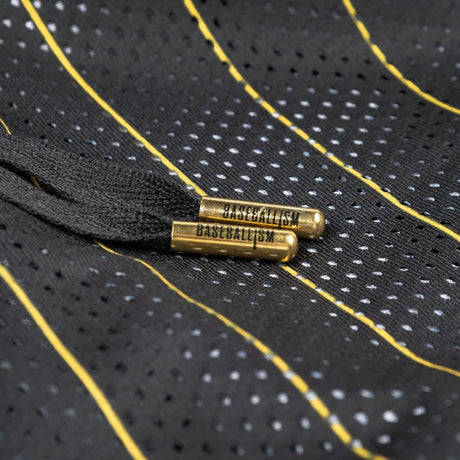 Close-up of a black mesh drawstring bag with yellow and white dotted stripes, featuring brass grommets engraved with the word 'GASTBULLISM'.