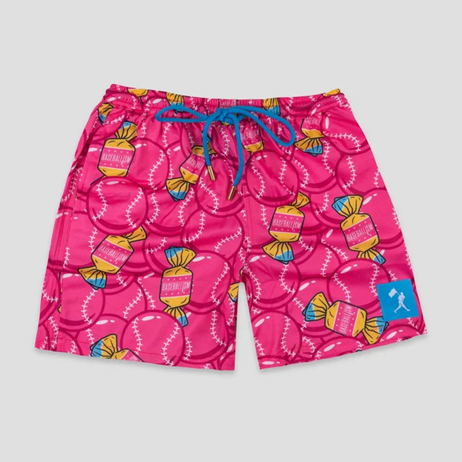 Bright pink shorts with a repeating pattern of baseballs and wrapped candy motifs, featuring a blue drawstring and a small blue logo patch on the lower right leg, shown against a neutral gray background.