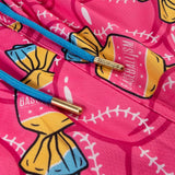 Close-up of a bright pink garment with a baseball-themed graphic print, featuring yellow and blue candy-like motifs, white baseball stitching details, and blue drawstrings with gold metal tips.