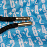 Close-up of black braided drawstring cords threaded through metallic gold eyelets engraved with the word 'BASEBALLISM', set against a blue fabric background patterned with white math equations.