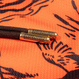 Close-up of a dark brown braided cord with two metallic gold-toned sliders engraved with the word 'BASEBALLISM', resting on an orange fabric background with a black graphic print.