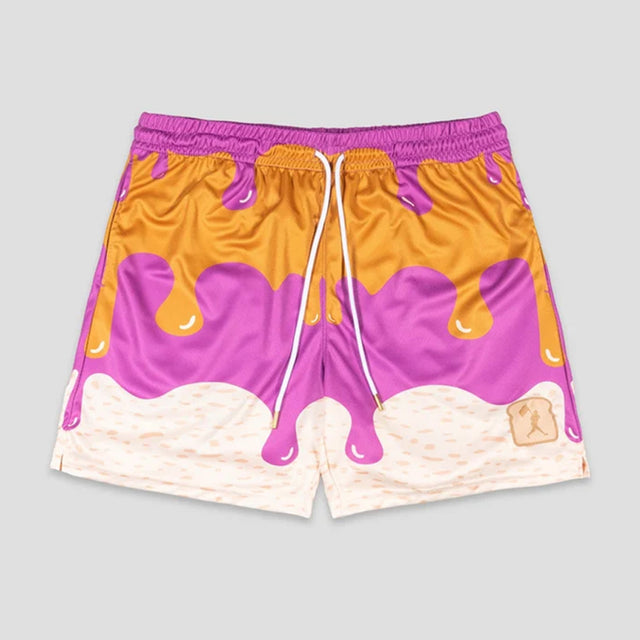A pair of kids athletic shorts featuring a colorful ice cream scoop dripping design in purple, orange, and cream, with a white drawstring and a small toast graphic on the lower right leg.