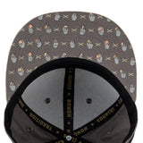 Close-up of the inside of a gray snapback cap with a repeating pattern of hand gestures and crossed X's, black mesh back panels, and black adjustable strap with gold text.