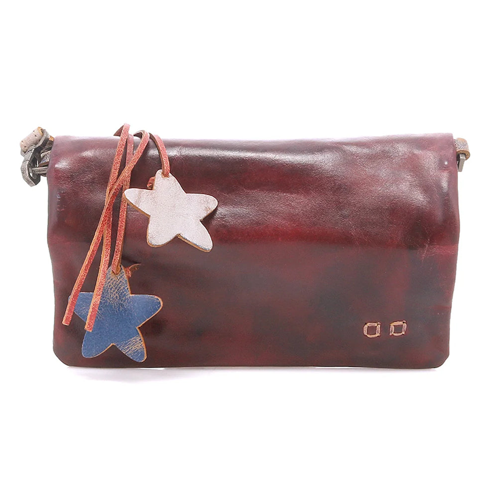 A dark reddish-brown leather clutch bag with a flap closure, featuring two hanging star-shaped charms (one light beige, one blue) on a leather strap, photographed against a plain white background.