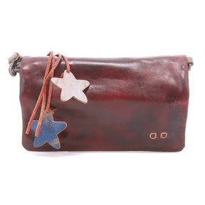A dark reddish-brown leather clutch bag with a flap closure, featuring two hanging star-shaped charms (one light beige, one blue) on a leather strap, photographed against a plain white background.