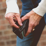 Close-up of hands opening a black wallet with a blurred brick wall background