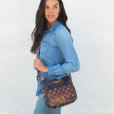 Woman holding a woven brown leather handbag against a white brick wall.