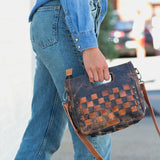 Person holding a checkered brown leather bag on a blurred street background