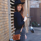 Woman wearing a black hat and carrying a brown leather bag against a brick wall.