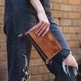 Person holding a brown leather wallet against a brick wall.