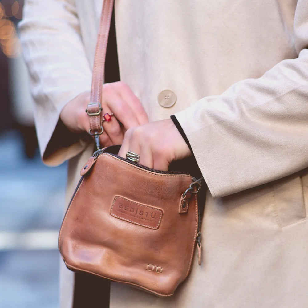 Person holding a brown leather purse with a visible brand logo, wearing a beige coat.