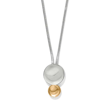 A modern two-tone pendant necklace featuring a silver snake chain, a large polished silver disc, and a small gold bead dangling below, set against a plain white background.
