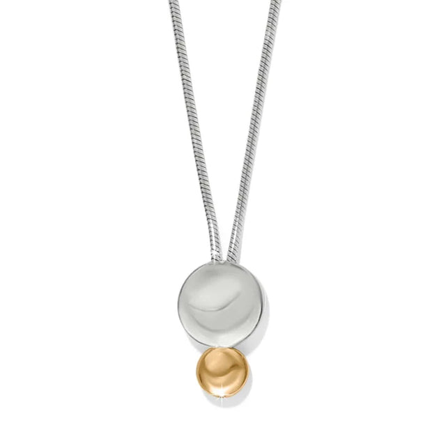 A modern two-tone pendant necklace featuring a silver snake chain, a large polished silver disc, and a small gold bead dangling below, set against a plain white background.