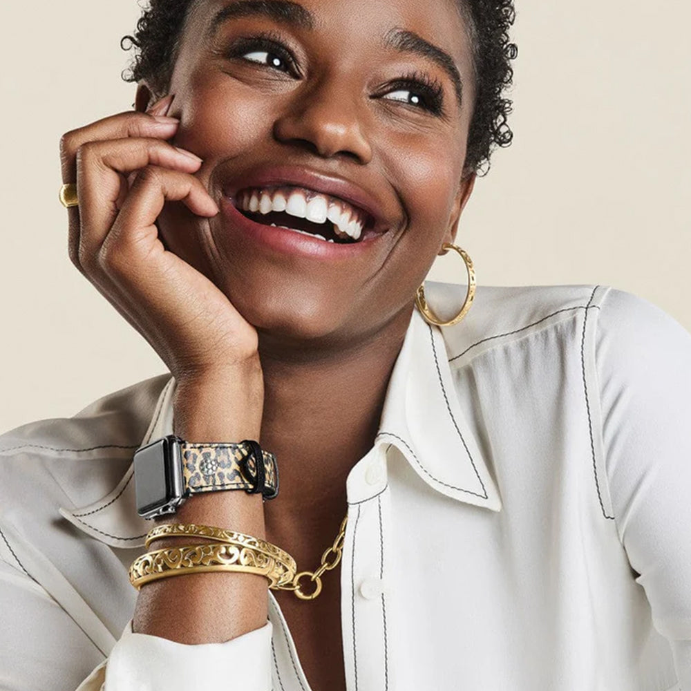 Woman wearing gold jewelry including a watch, bracelet, and earrings on a beige background