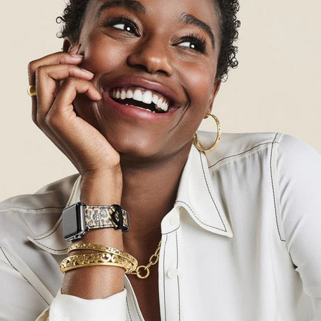Woman wearing gold jewelry including a watch, bracelet, and earrings on a beige background