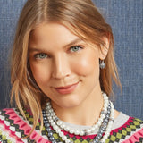 Woman wearing multiple necklaces with a patterned sweater against a blue denim background