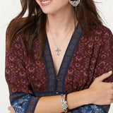 Woman wearing a patterned top with a cross necklace and bracelet on a white background