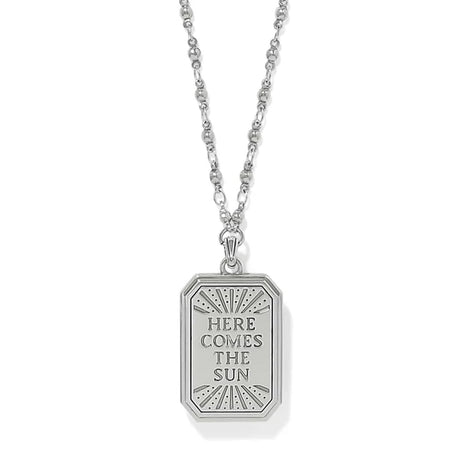A silver pendant necklace featuring a rectangular tag-style pendant with the engraved text 'HERE COMES THE SUN' and a sunburst design, shown on a white background.
