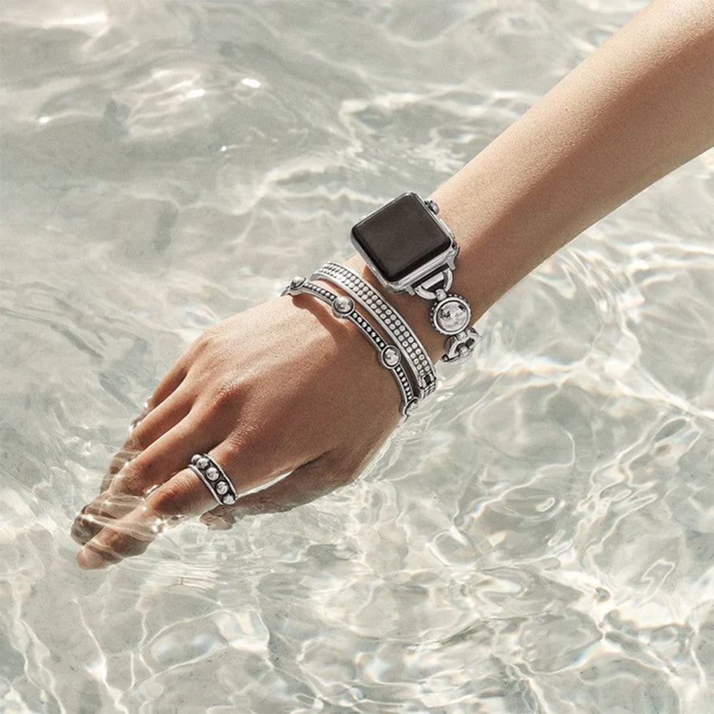 Hand with silver watch and bracelets by clear water