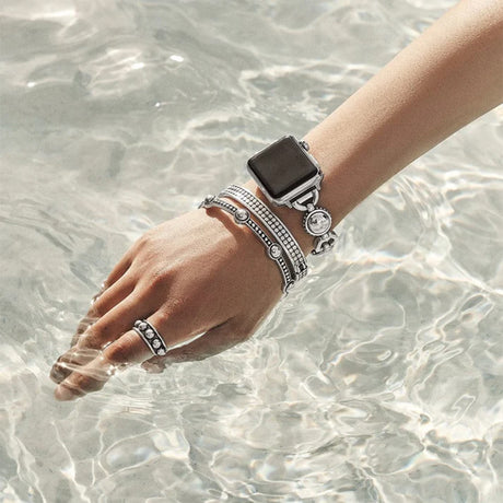 Hand with silver watch and bracelets by clear water