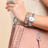 Hand wearing a silver watch and bracelet on a pink handbag against a beige background
